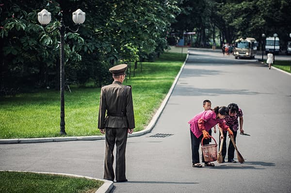 Street sweepers keep Pyongyang’s streets clean under the watchful eye of a solider