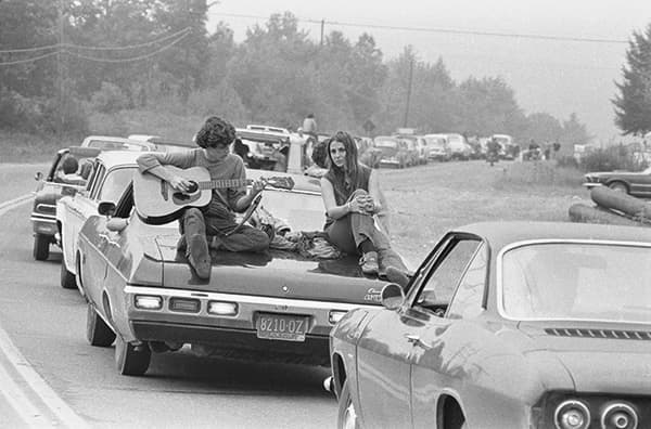 A couple play the guitar sitting on their car on the way to the Woodstock Festival, August 1969